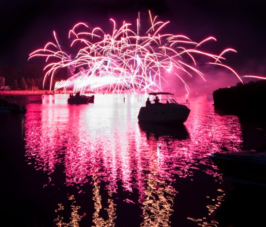 Photo of colorful, exploding fireworks in the night sky during a July 4th holiday celebration in Toledo Ohio Taken  along the Maumee river with boats and colorful reflections in the water.